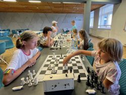 Uczestnicy klubu w sali biblioteki siedzą przy stolach oraz szachownicach podczas rozgrywek szachowych