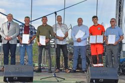 Grupa siedmiu mężczyzn stojących na scenie. Wszystkie osoby trzymają wręczone podziękowania od Wójta Gminy.