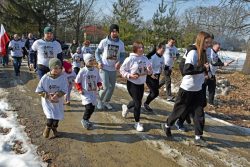 Uczestnicy biegu „Tropem Wilczym” – dzieci i dorośli – biegną wspólnie leśną drogą, ubrani w okolicznościowe koszulki.