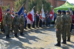 Poczet sztandarowy oraz młodzież w mundurach polowych prezentują postawę zasadniczą przed rzędami sztandarów podczas uroczystych obchodów biegu „Tropem Wilczym”.