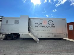 Mammobus „Moja Mammografia” zaparkowany przed budynkiem, w słoneczny dzień pod błękitnym niebem.
